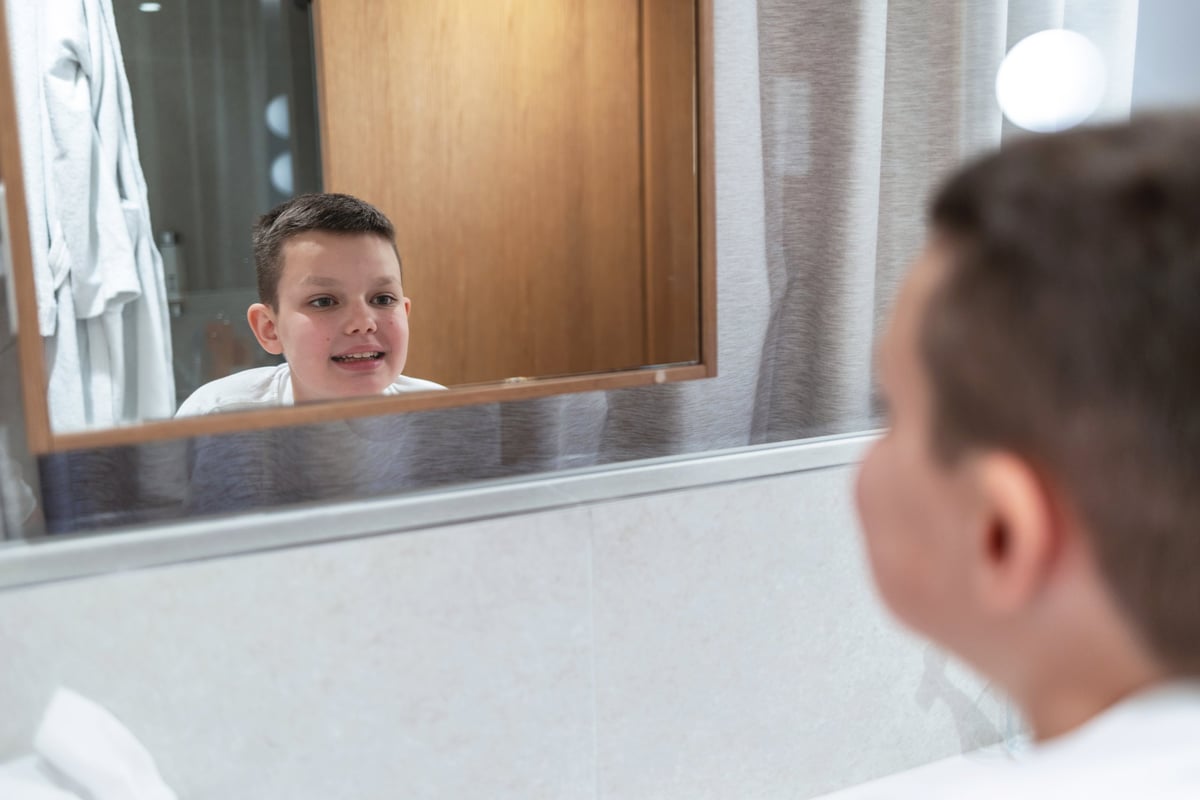 Shot of a little boy checking his teeth in the mirror at home. Cute 10 years old boy washing teeth in bathroom looking in mirror and smiling.