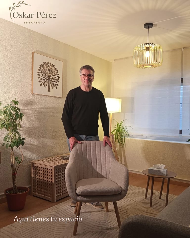 Man standing in modern therapy office with beige armchair, potted plants, pendant light, and Oskar Perez Terapeuta branding